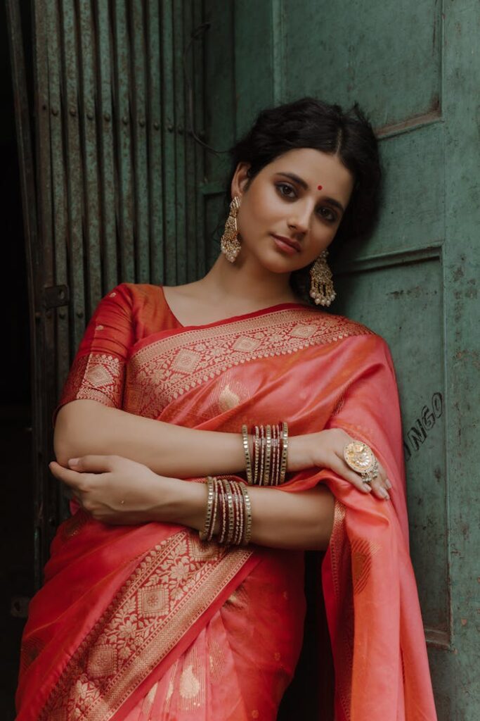 Woman in red saree with gold jewelry poses gracefully outdoors.