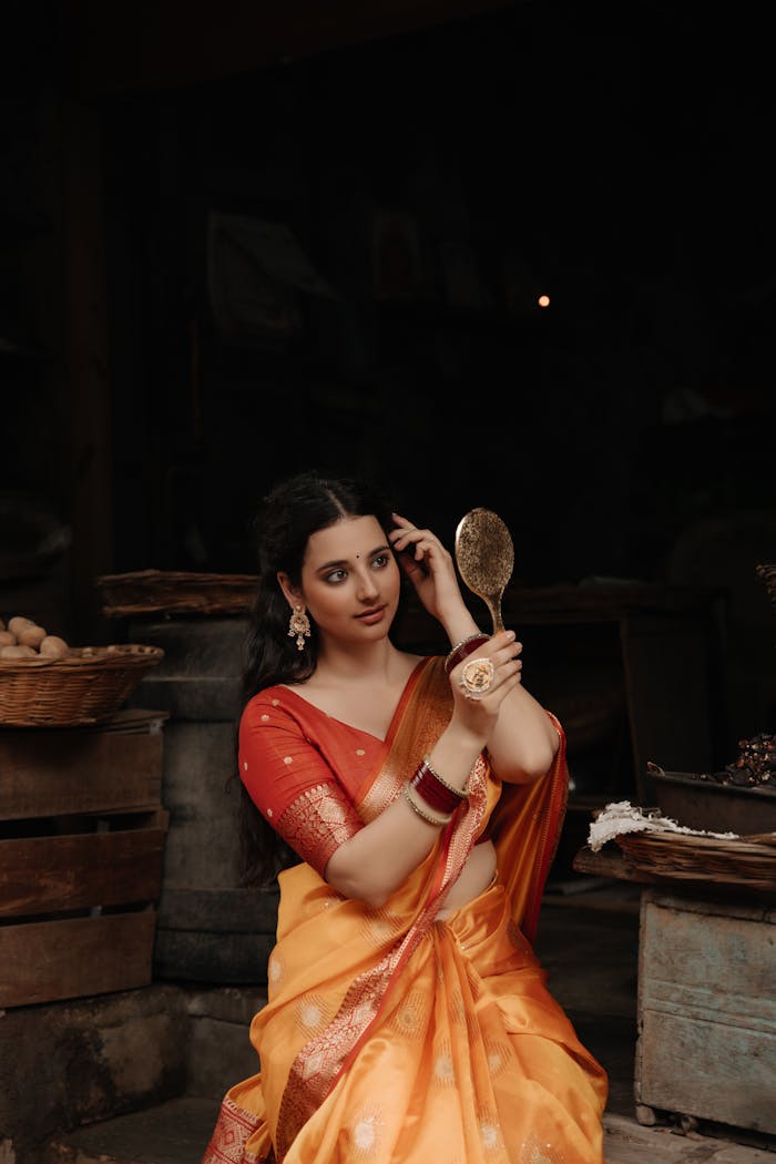 Woman in a beautiful saree admiring herself in a mirror, surrounded by rustic decor.