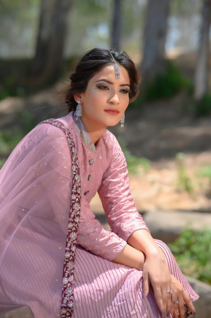 Elegant portrait of a woman in traditional pink attire with intricate jewelry in an outdoor setting.
